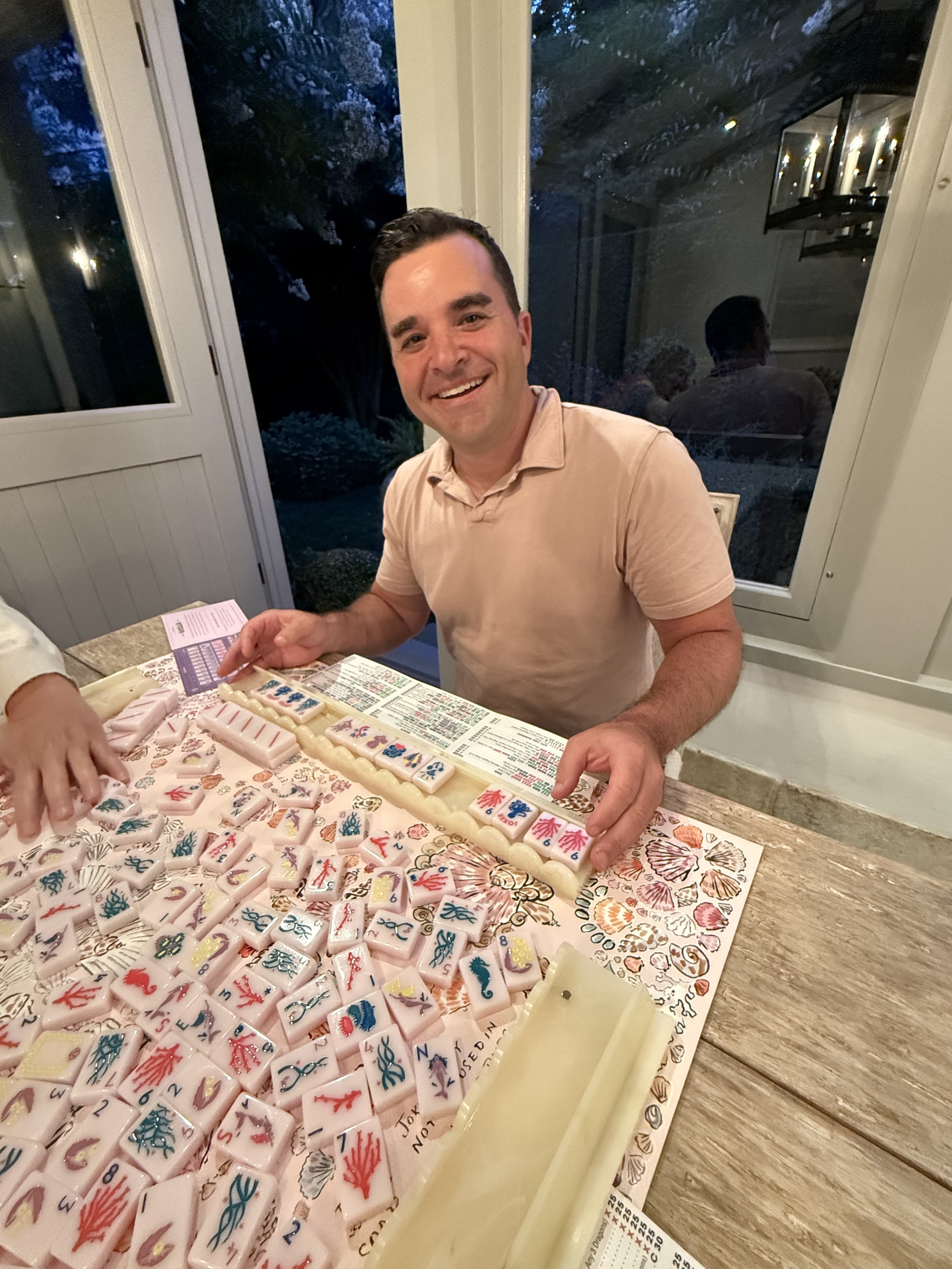 Smiling man holding a Mahj cap at a mahjong table